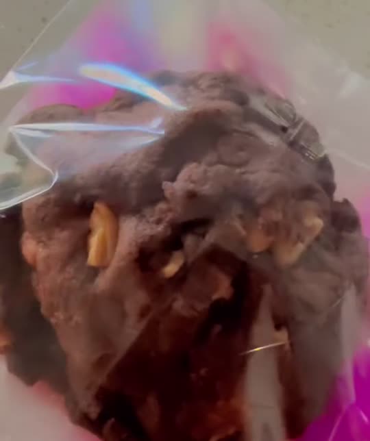 A freshly wrapped chocolate cookie held up in a pink-gloved hand